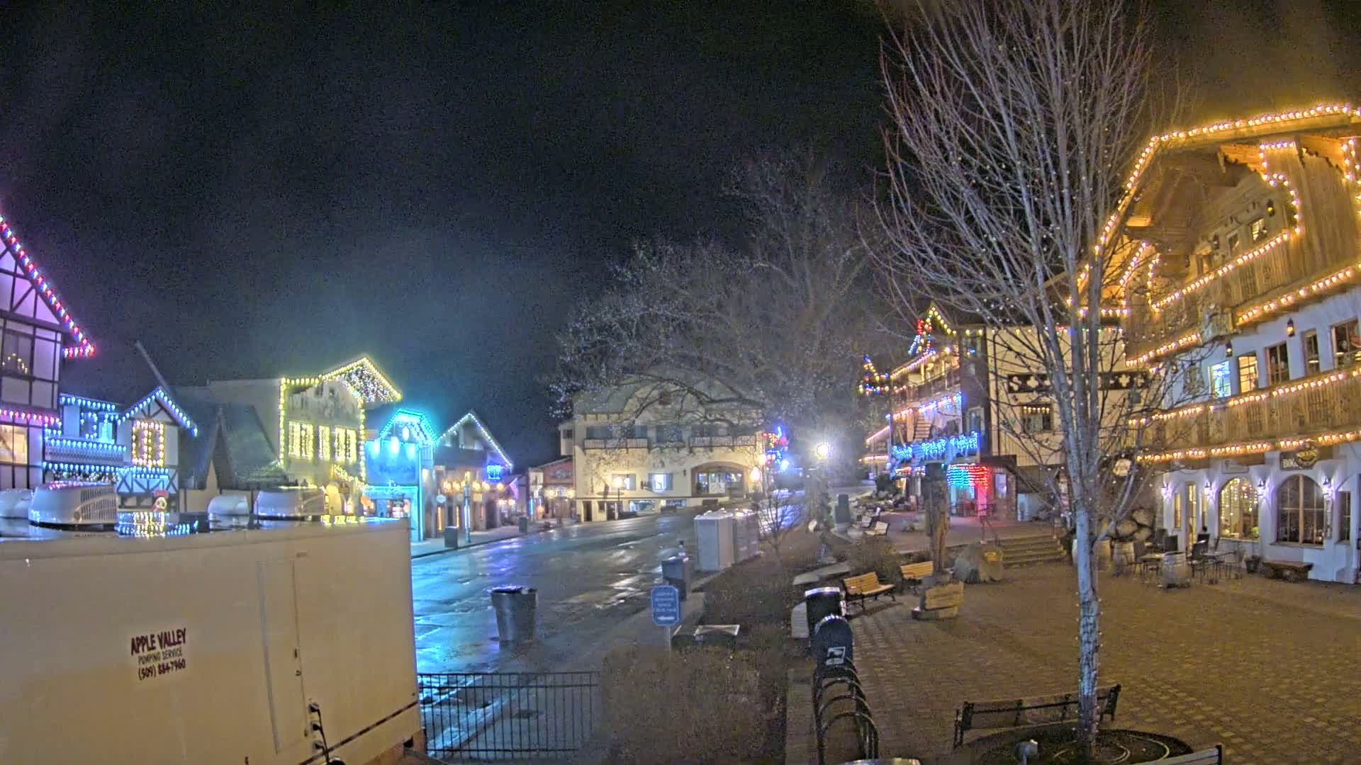 A nighttime scene of a town square with several buildings decorated with colorful lights, under a dark sky.
