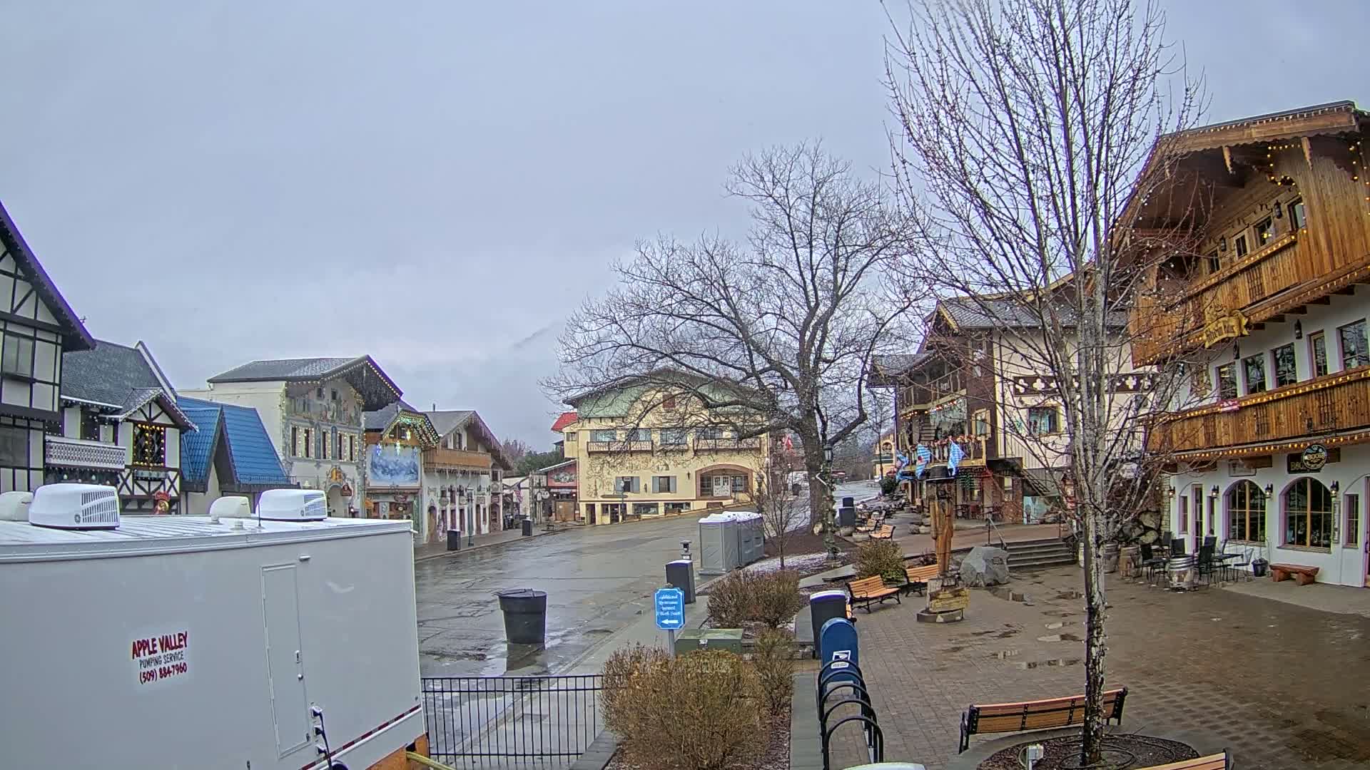 A town square with several buildings in a European style is seen on an overcast day with wet pavement.