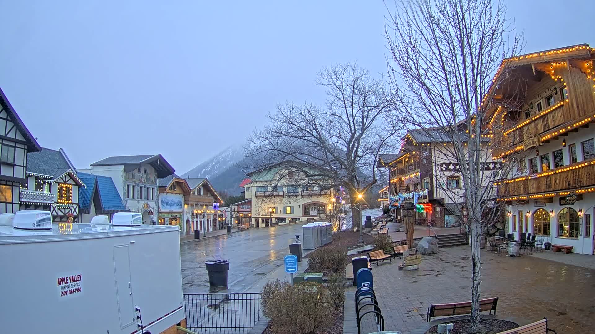 A wet town square with several European-style buildings and a mountain in the background under an overcast sky.