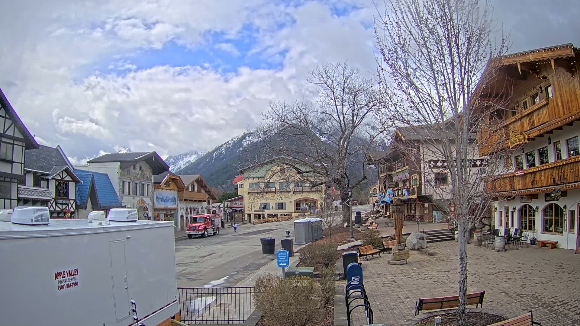 A partly cloudy day reveals a quaint village of European-style buildings nestled at the foot of snow-capped mountains.