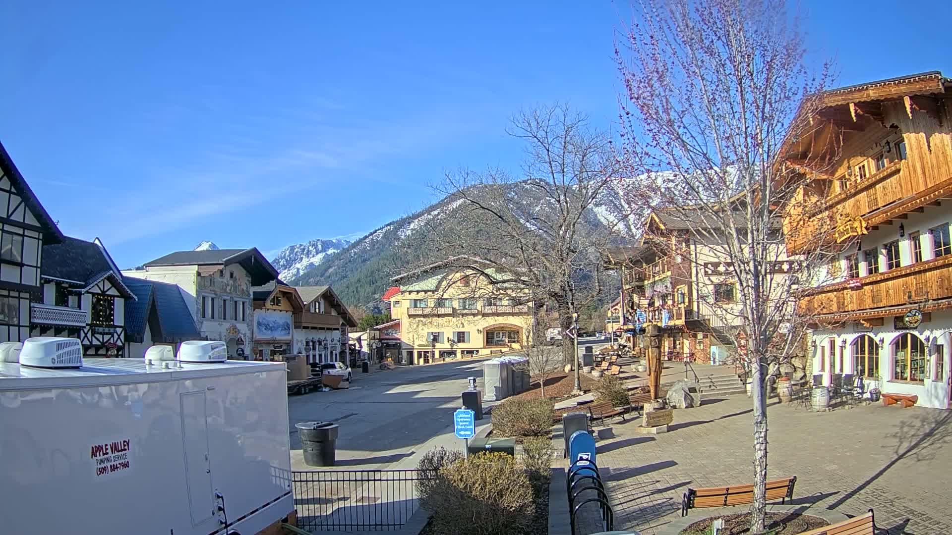 A sunny day in a Bavarian-style village square nestled against snow-capped mountains.