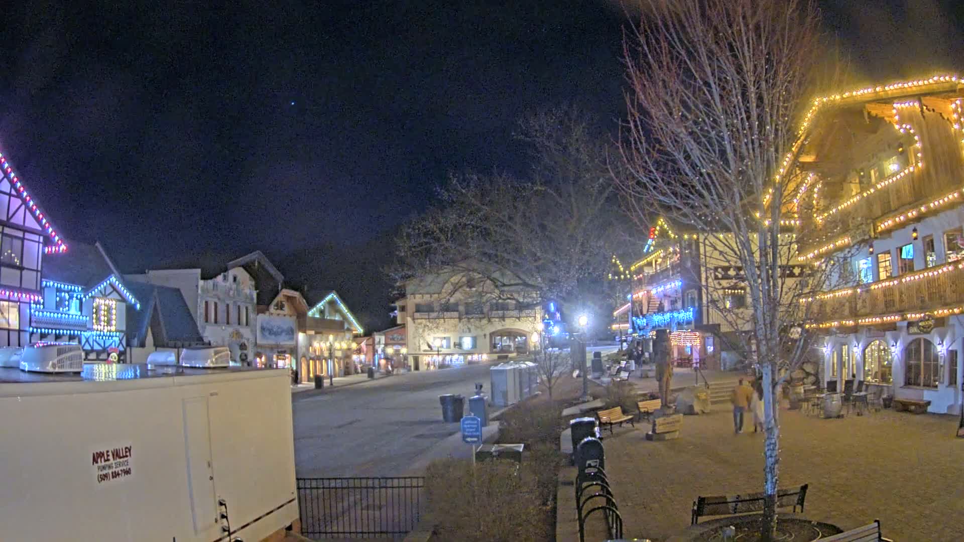 A nighttime scene of a town square with buildings decorated with Christmas lights, under a clear, dark sky.