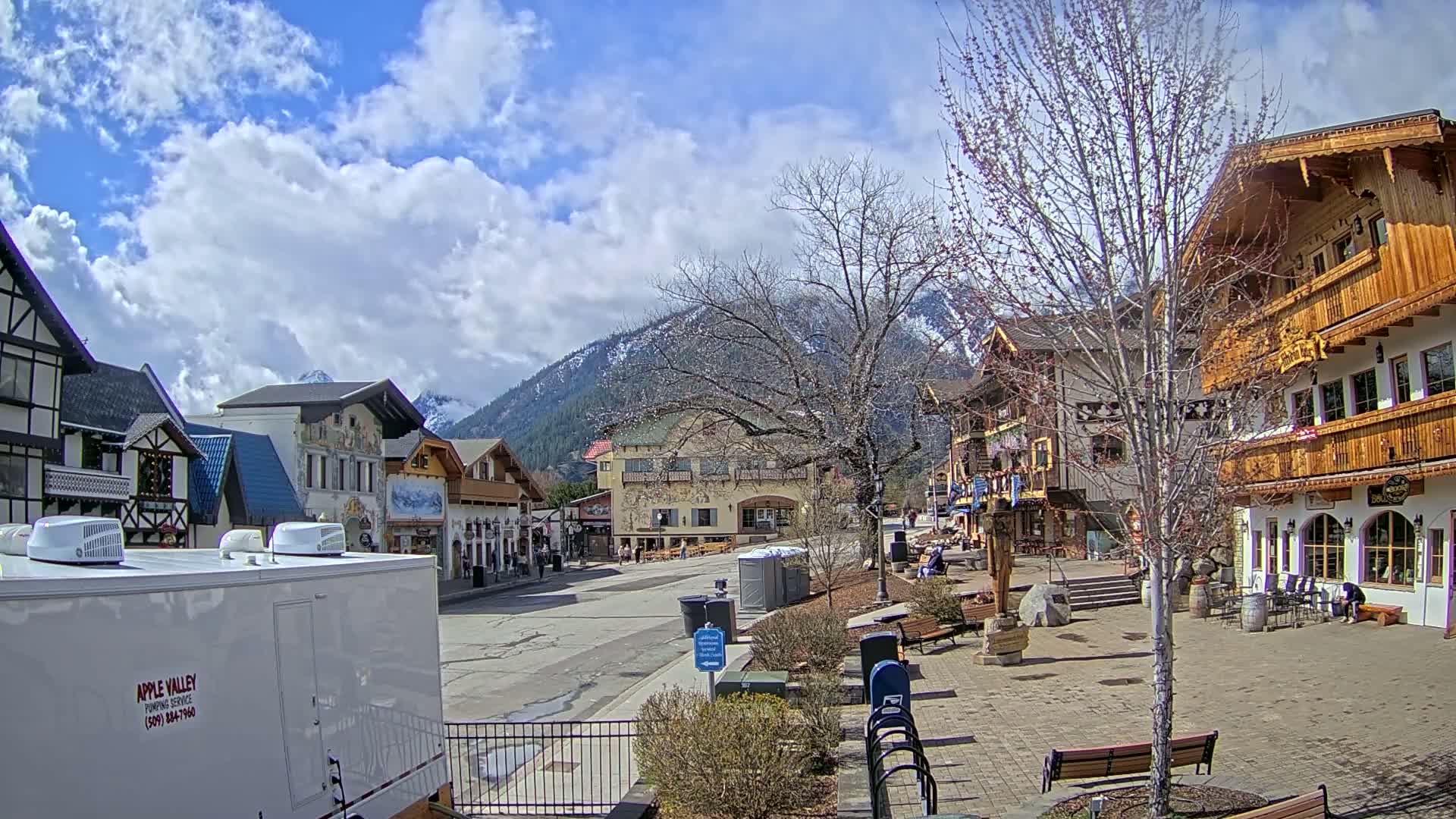 A partly cloudy day reveals a village of European-style buildings nestled at the base of a snow-capped mountain range.