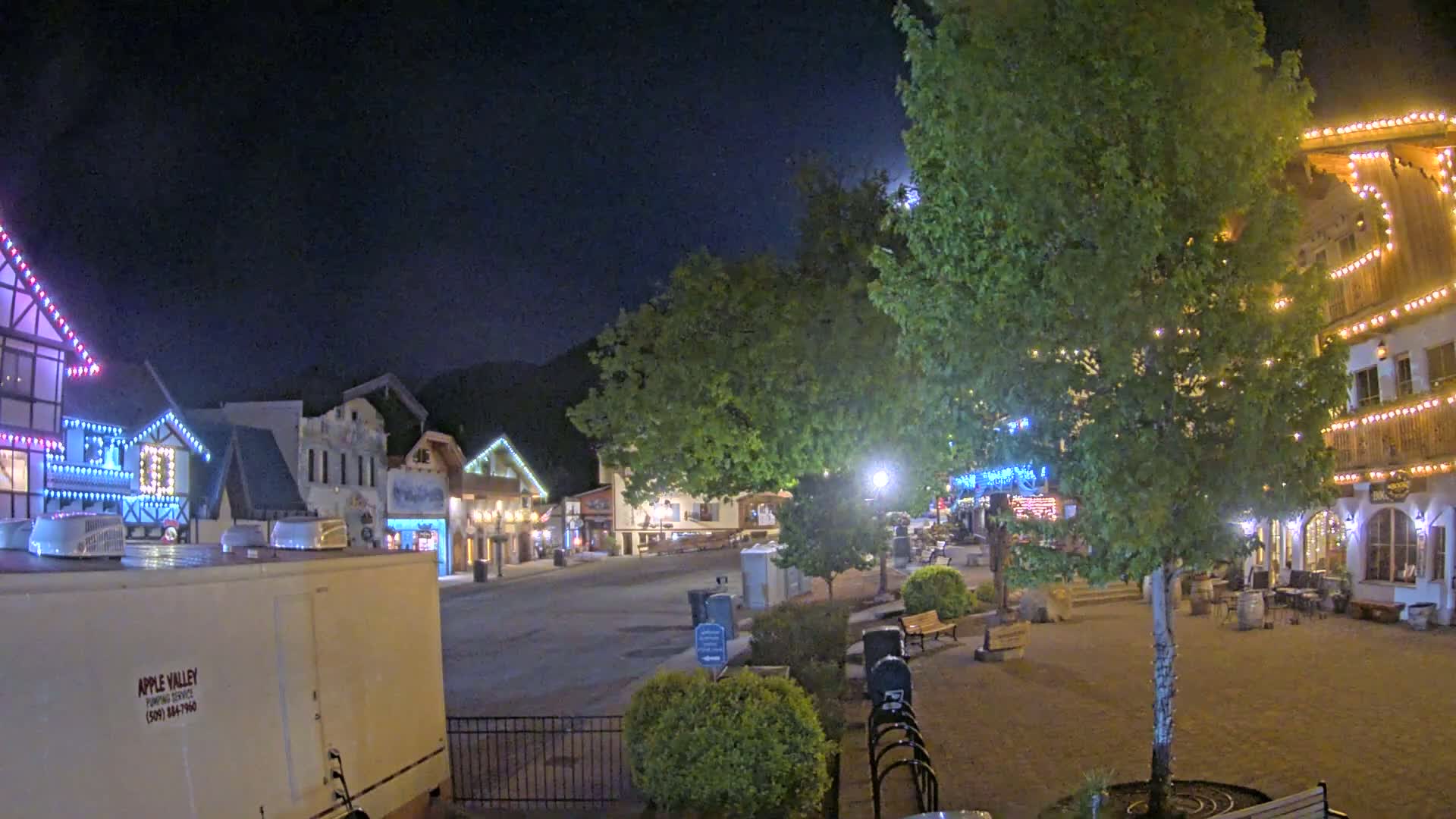 A nighttime scene of a town square with buildings decorated with string lights, under a clear sky.
