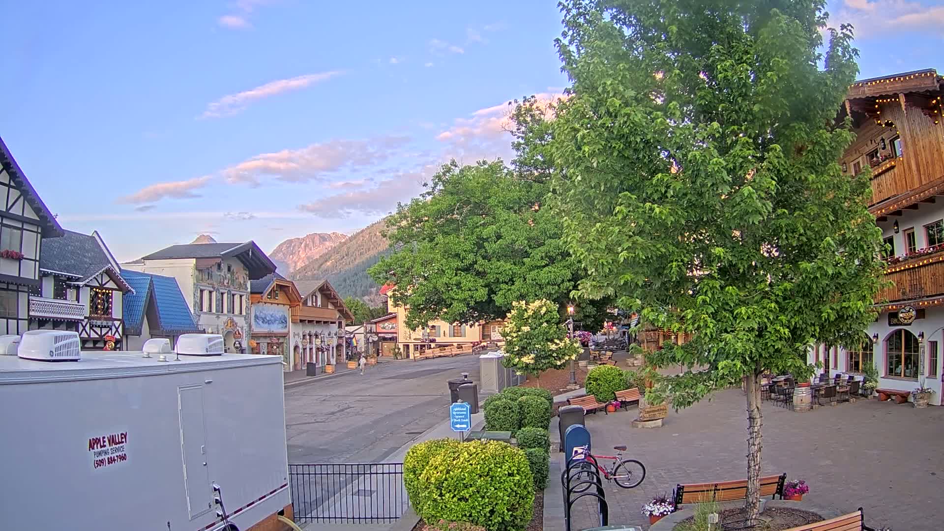 A mostly empty town square with several European-style buildings, under a partly cloudy evening sky, sits against a backdrop of mountains.