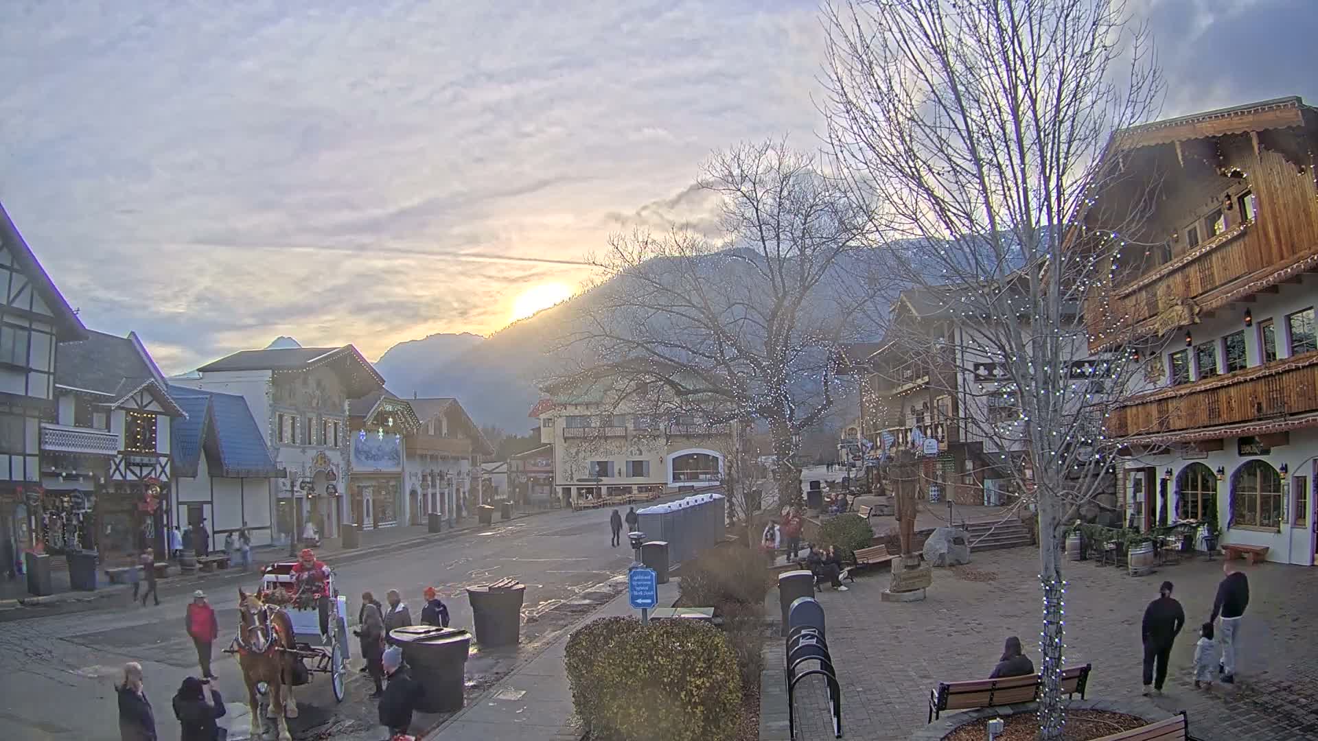 A picturesque Bavarian-style town square is brightly illuminated at night with numerous colorful holiday lights adorning buildings and trees under a clear, dark sky.
