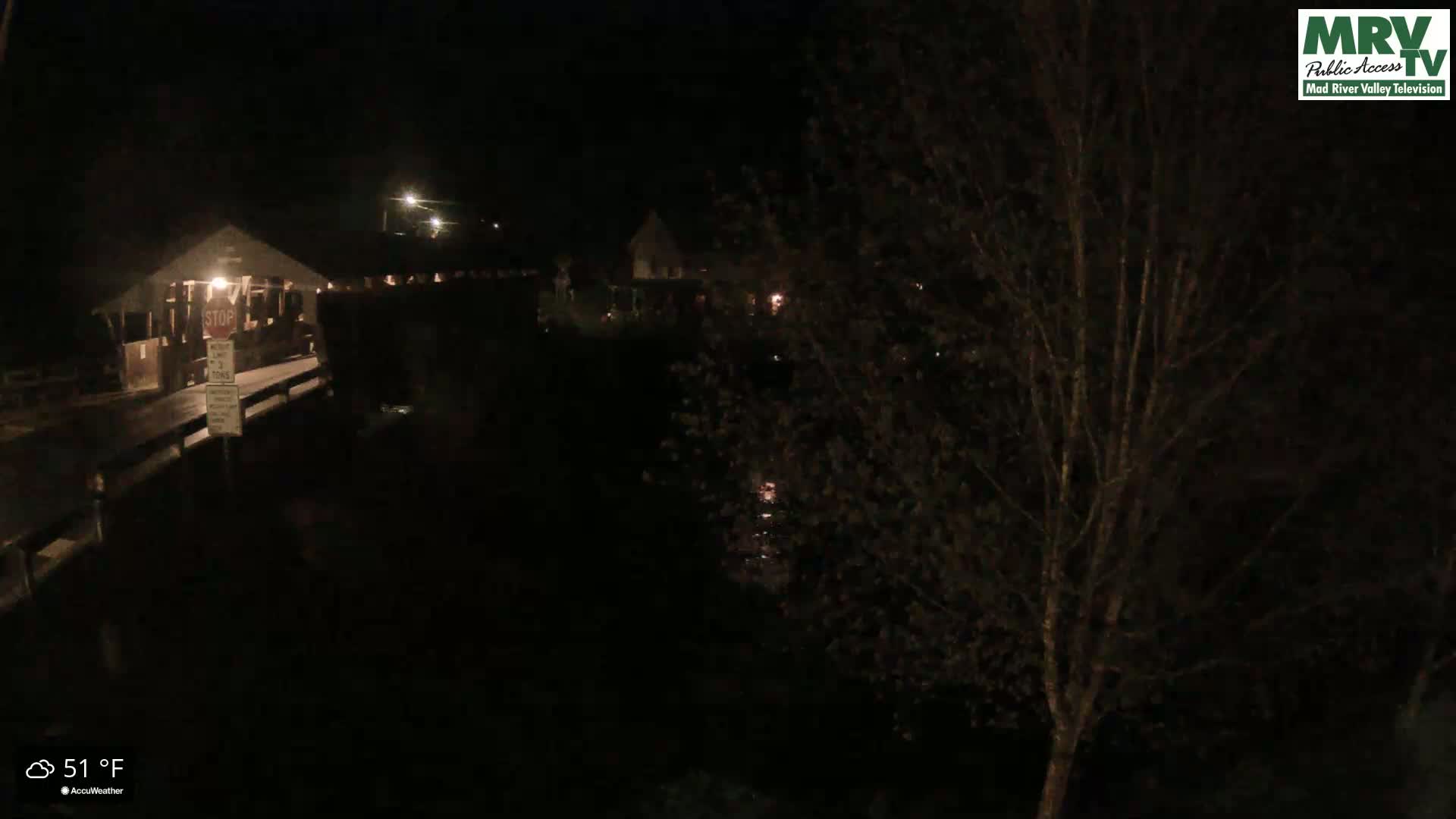 A nighttime view of a dark bridge and surrounding area, illuminated by a few lights, with a temperature of 51°F.