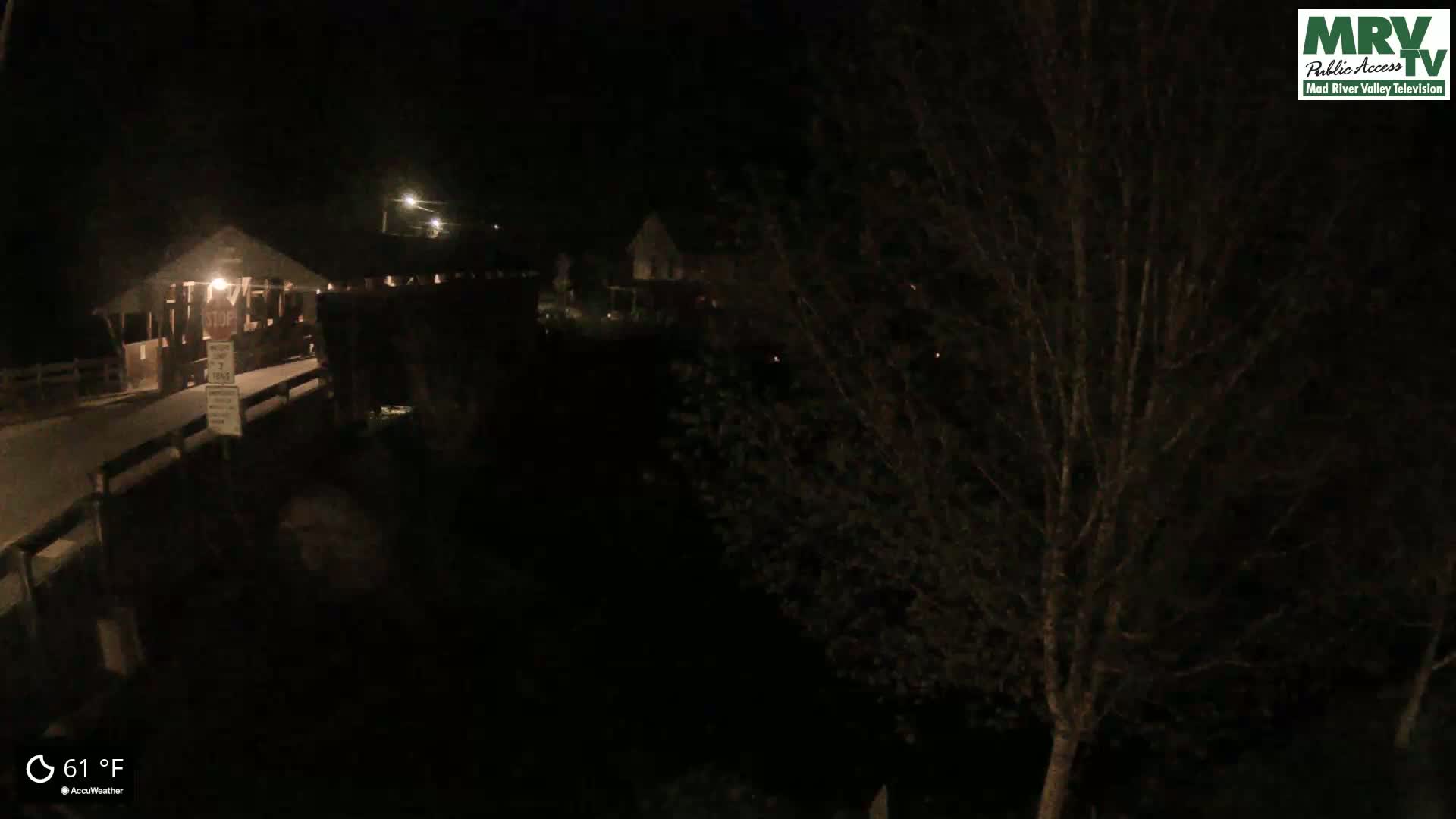 A nighttime view of a covered bridge and surrounding area at 61°F, with dark trees obscuring some of the view.