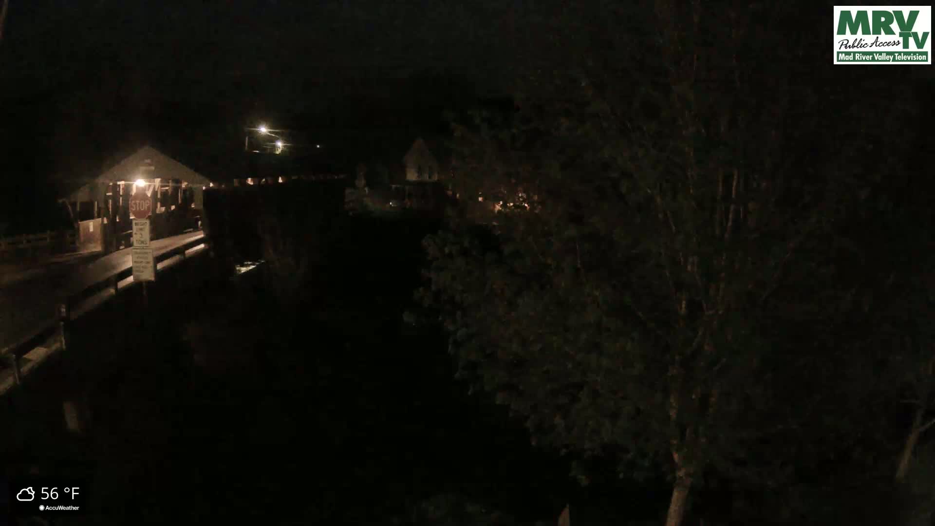 A nighttime view of a covered bridge, partially obscured by trees, with a temperature of 56 degrees Fahrenheit.