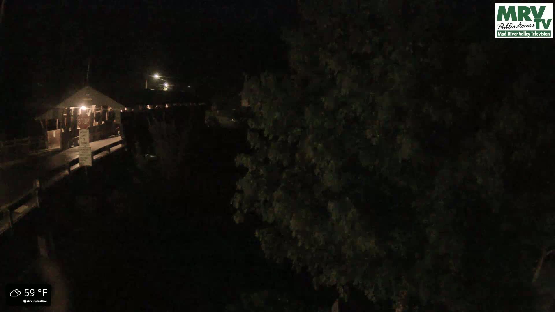A nighttime view of a covered bridge and surrounding trees at 59°F.
