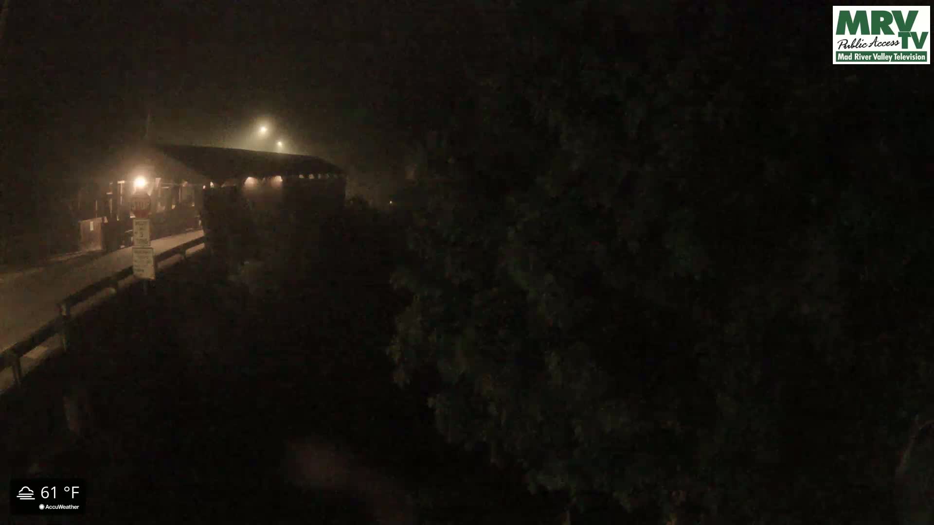 A covered bridge is dimly lit at night in foggy conditions.