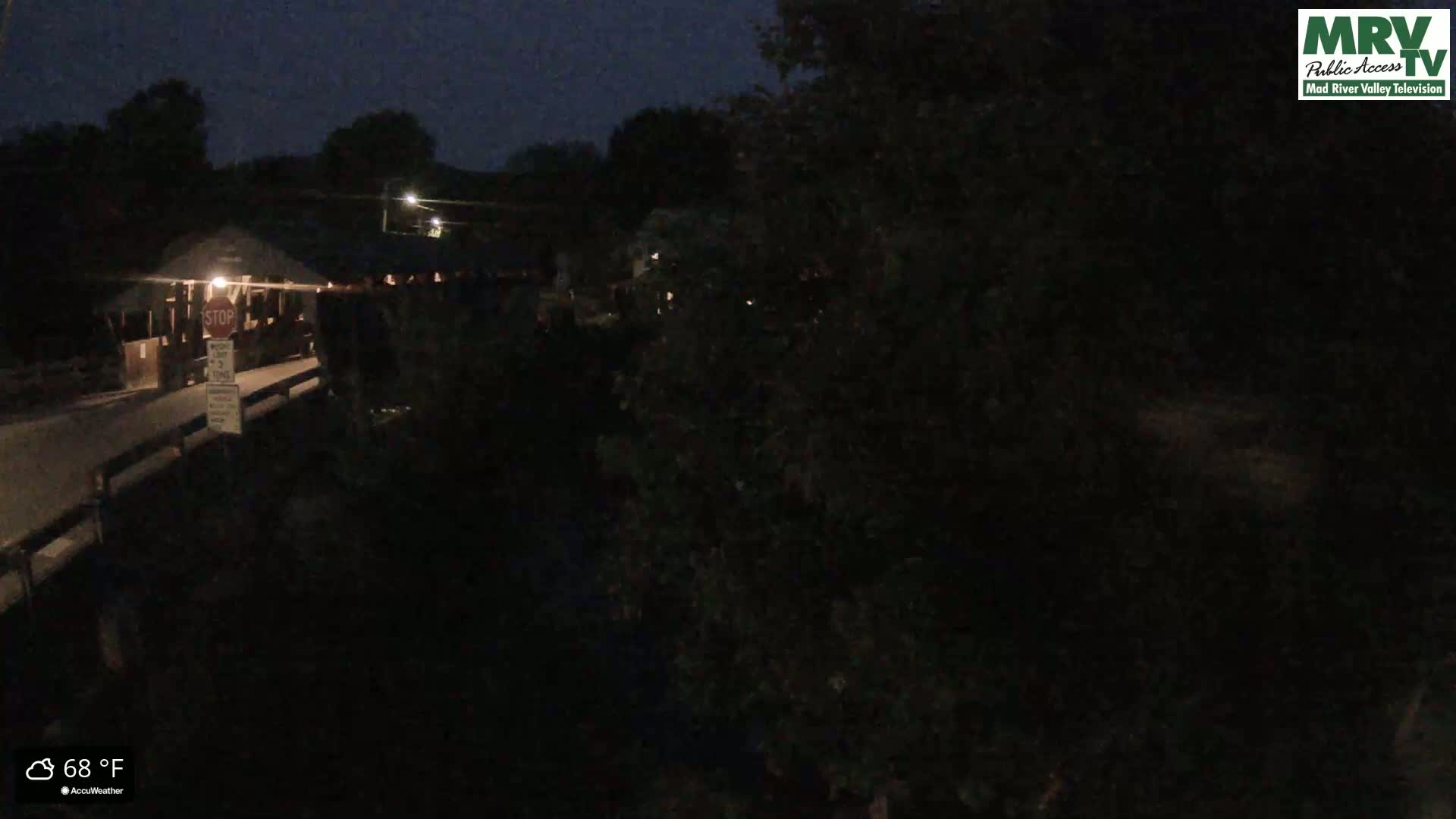 A nighttime view of a covered bridge and surrounding dark trees under a clear, dark sky.