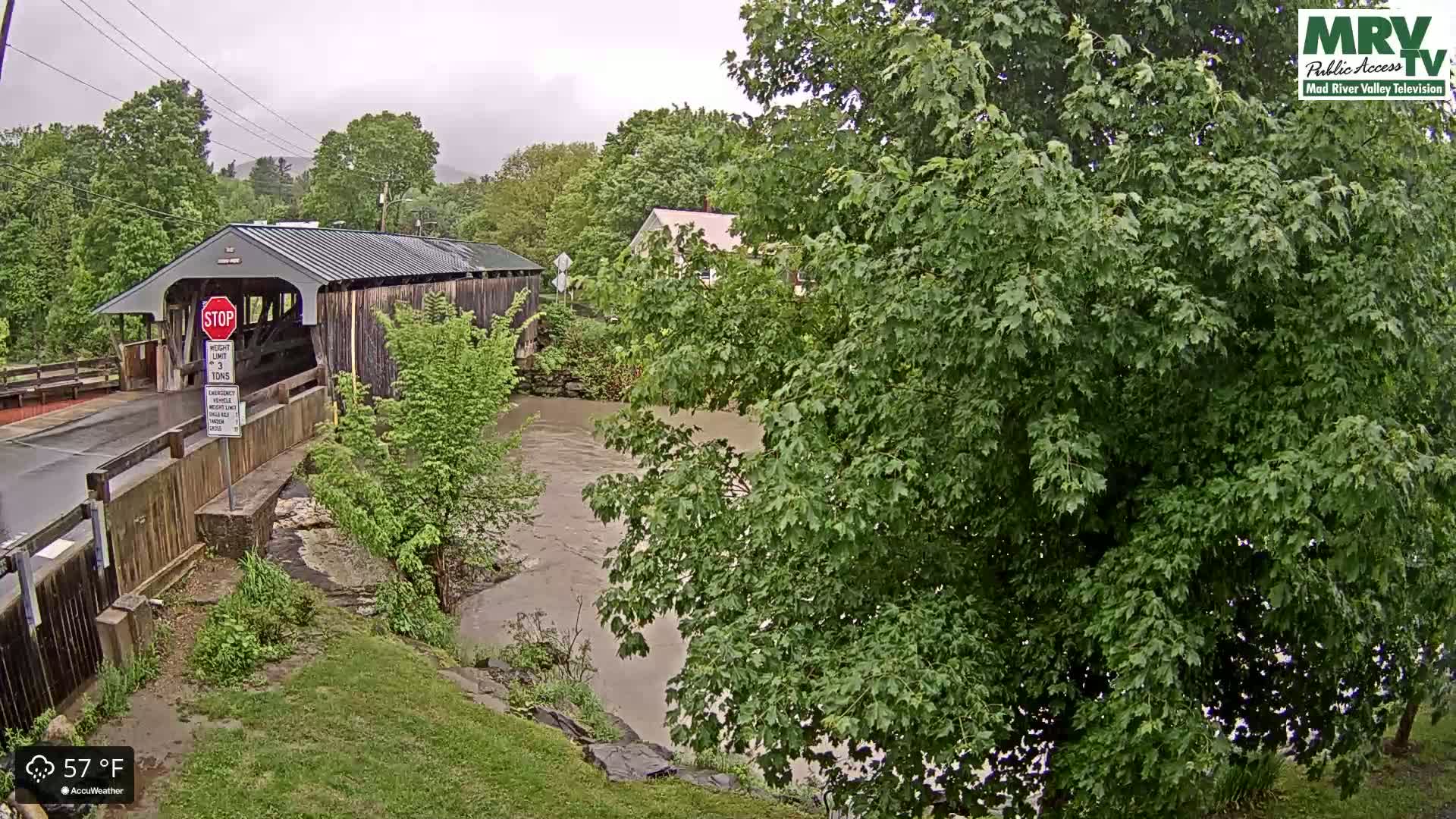 A covered bridge spans a muddy river under an overcast sky.