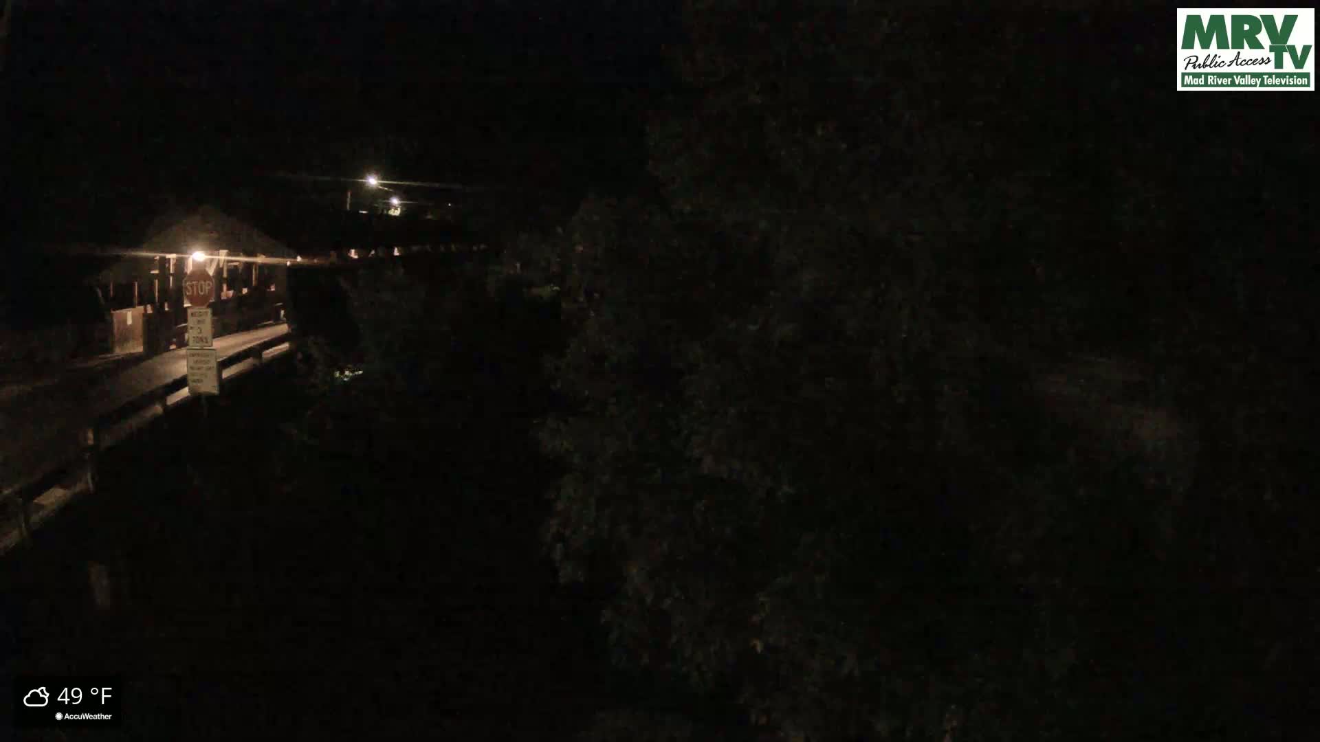 A nighttime view of a bridge and surrounding dark foliage at 49°F.