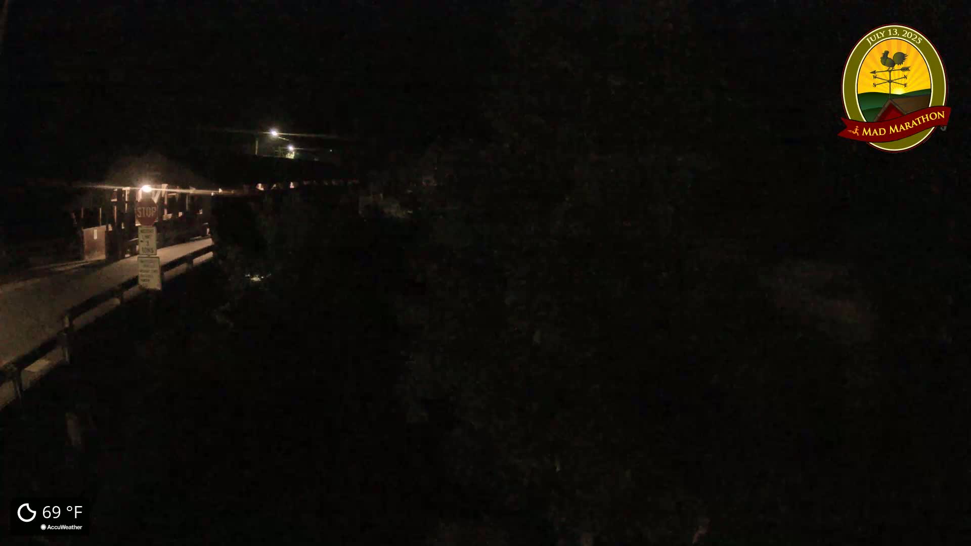 A nighttime, overhead view of a dark, empty road leading to a stop sign at a bridge, with a temperature of 69°F.