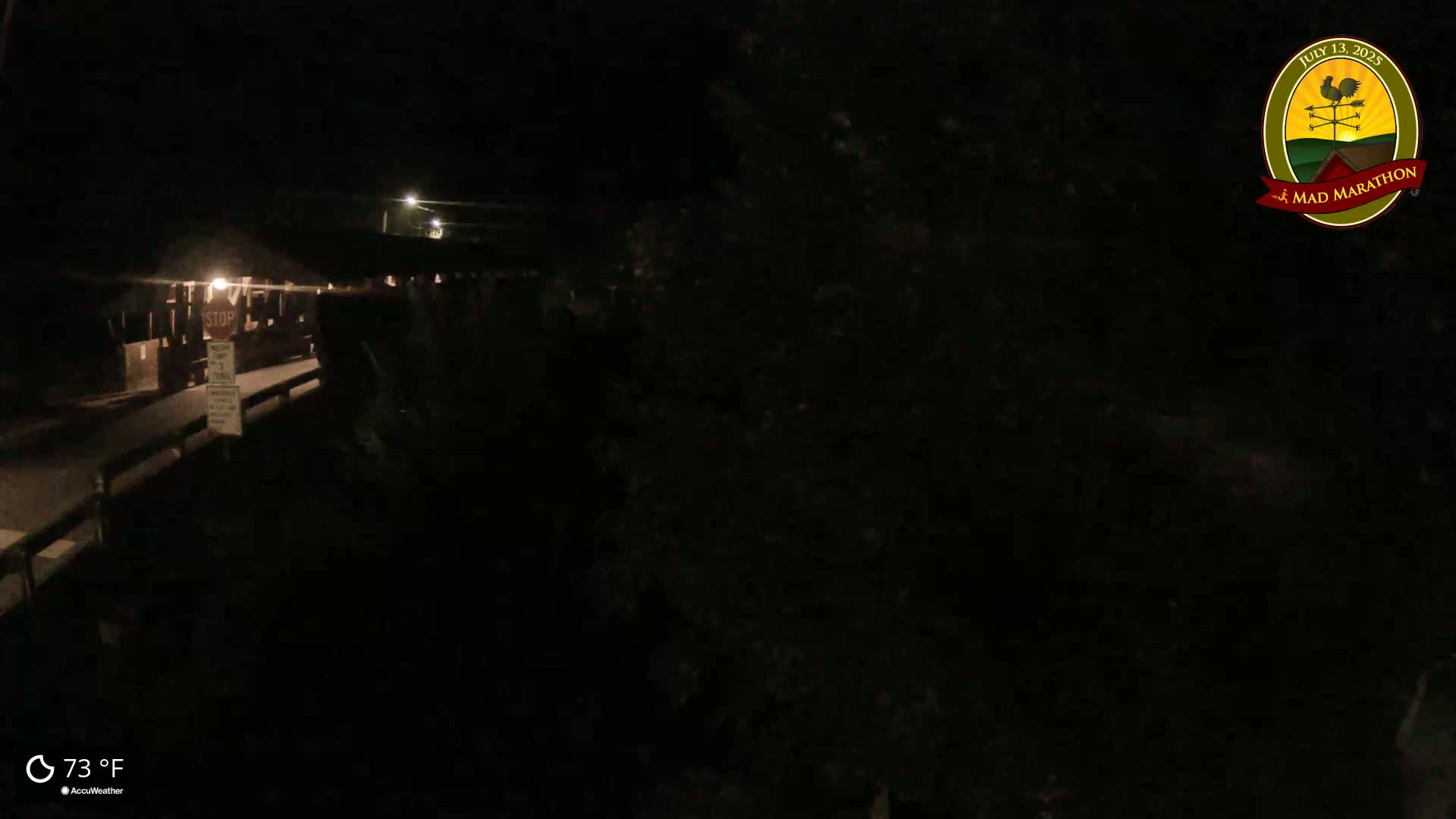 A nighttime, dimly lit view of a roadway with a stop sign and a walkway leading to a covered structure under a dark sky.