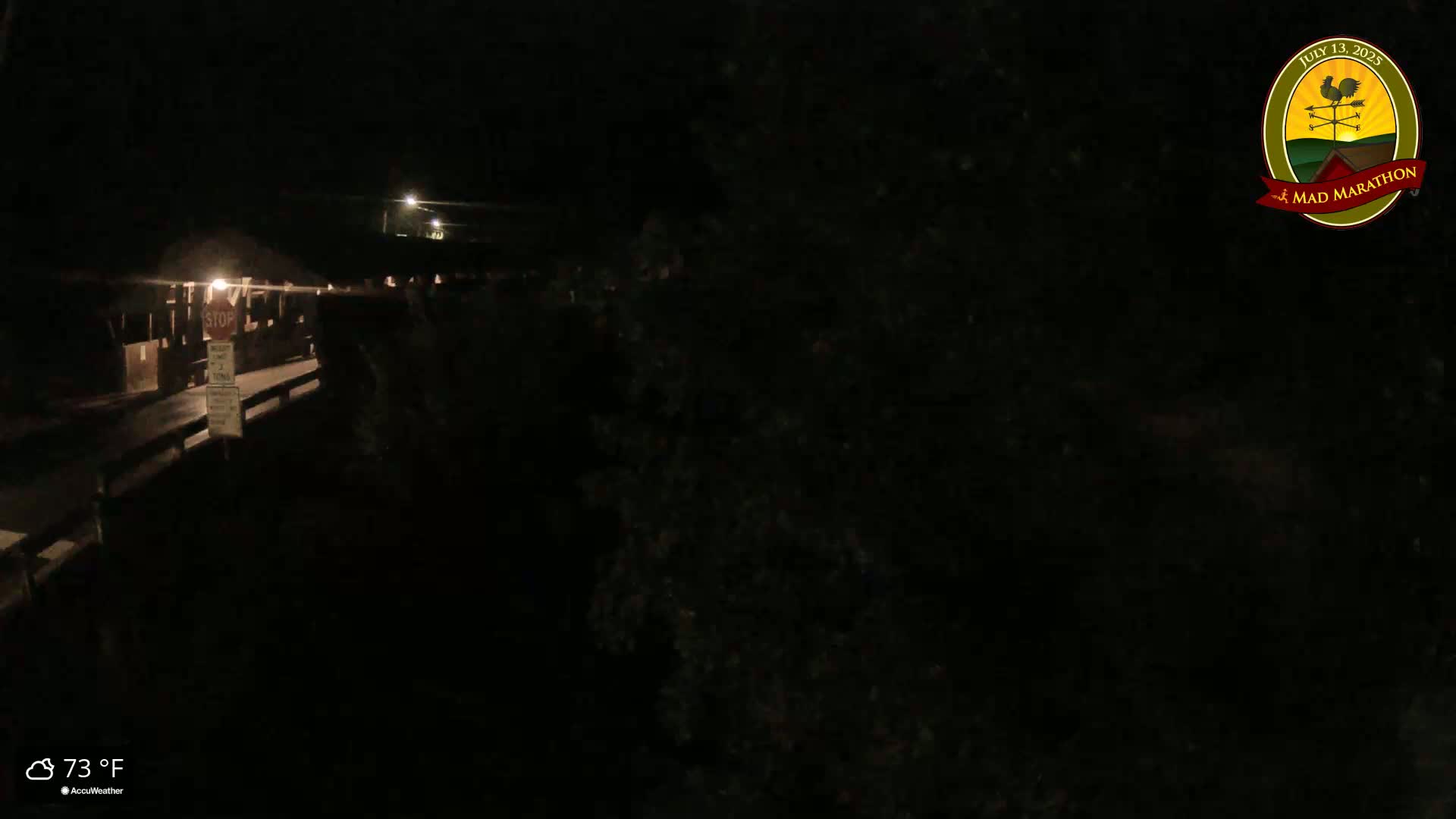 A dimly lit nighttime scene shows a bridge with a stop sign, sparsely populated with shadowy figures, under a dark sky at 73°F.