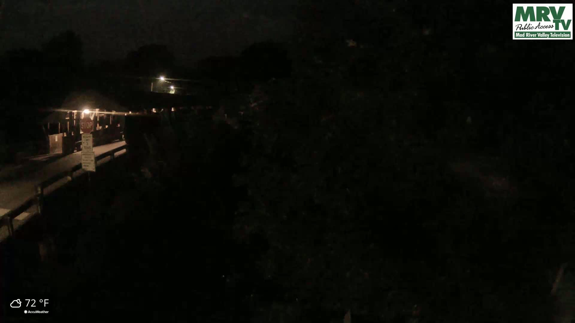 A nighttime view of a dark, mostly obscured covered bridge with a stop sign visible, under a clear sky at 72°F.