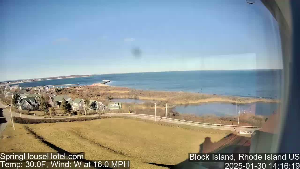 A coastal view shows a calm ocean under a clear blue sky, with houses and a marshy area in the foreground, and a 30°F temperature and a 16 mph westerly wind.