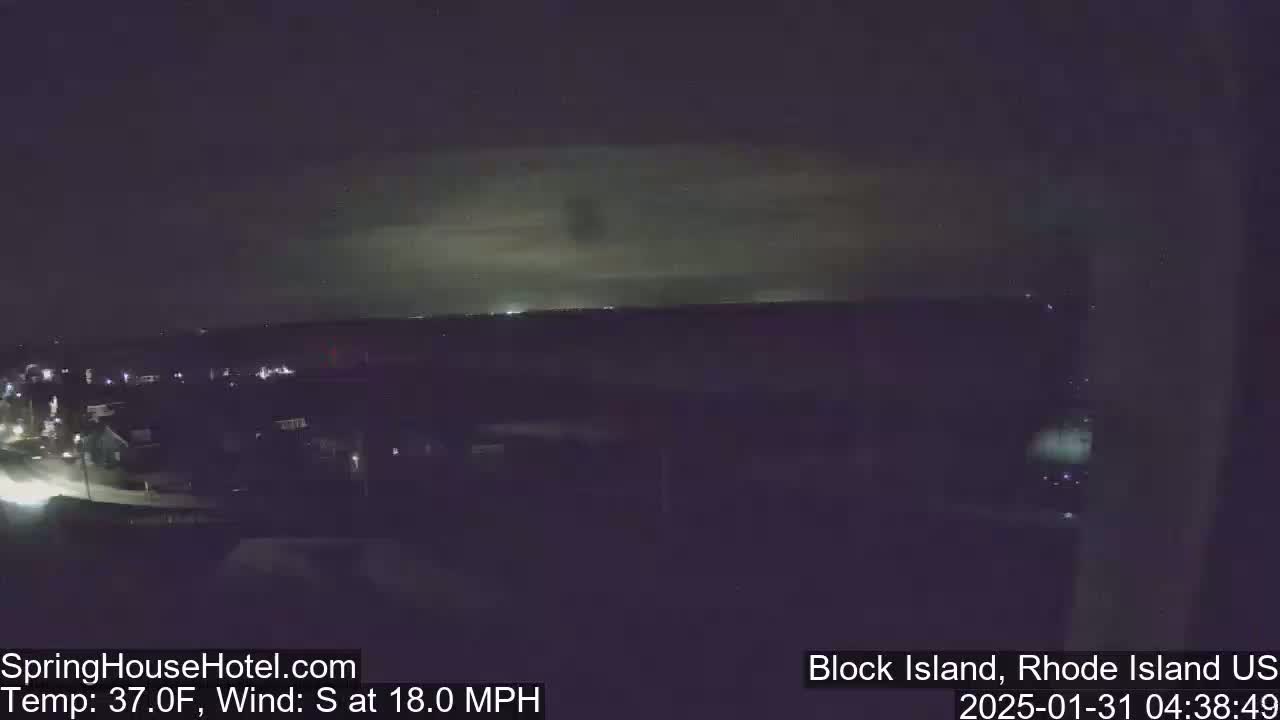 A nighttime view of a town lit by streetlights under a dark sky with a faint, greenish glow on the horizon, and a south wind blowing at 18 mph.
