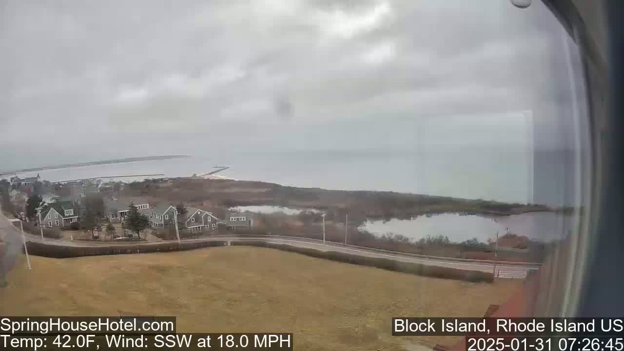 A coastal view on an overcast day shows a calm body of water, a small town, and a marshy area with a road winding through it.