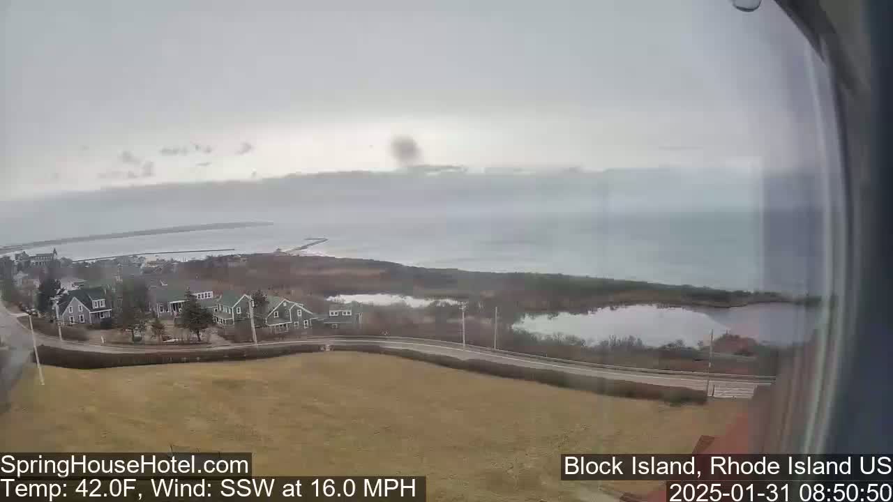 A coastal view on an overcast day shows a small town nestled near the water, with a calm body of water extending to the horizon.