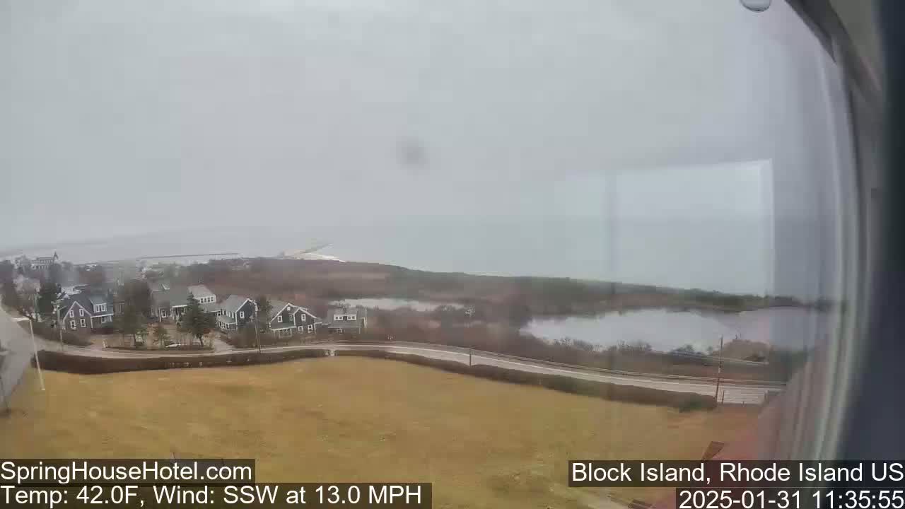A coastal view shows houses and a body of water under an overcast sky with a south-southwest wind at 13 miles per hour.