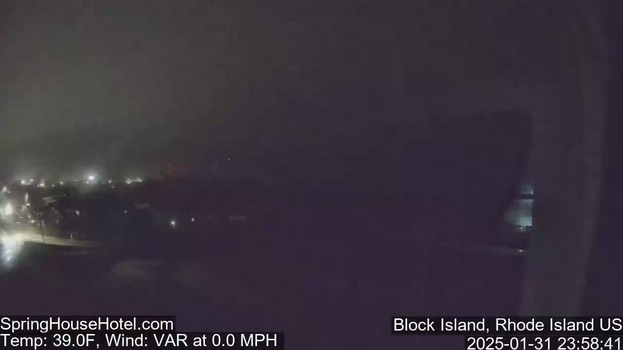 A nighttime, foggy view of a town with faint lights, showing a calm, 39°F atmosphere with no wind.
