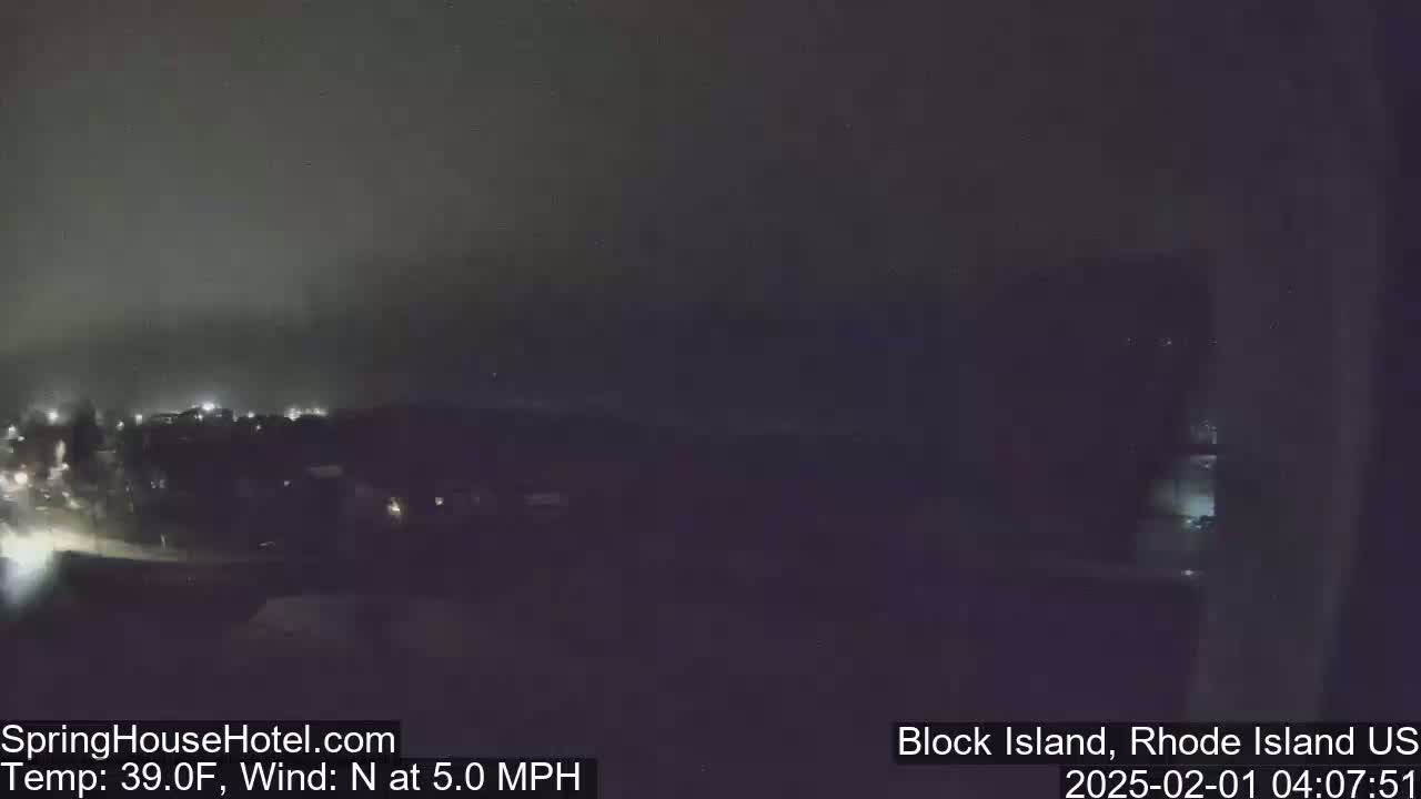 A nighttime view of dimly lit buildings and a dark, hazy sky with a 5.0 mph north wind.
