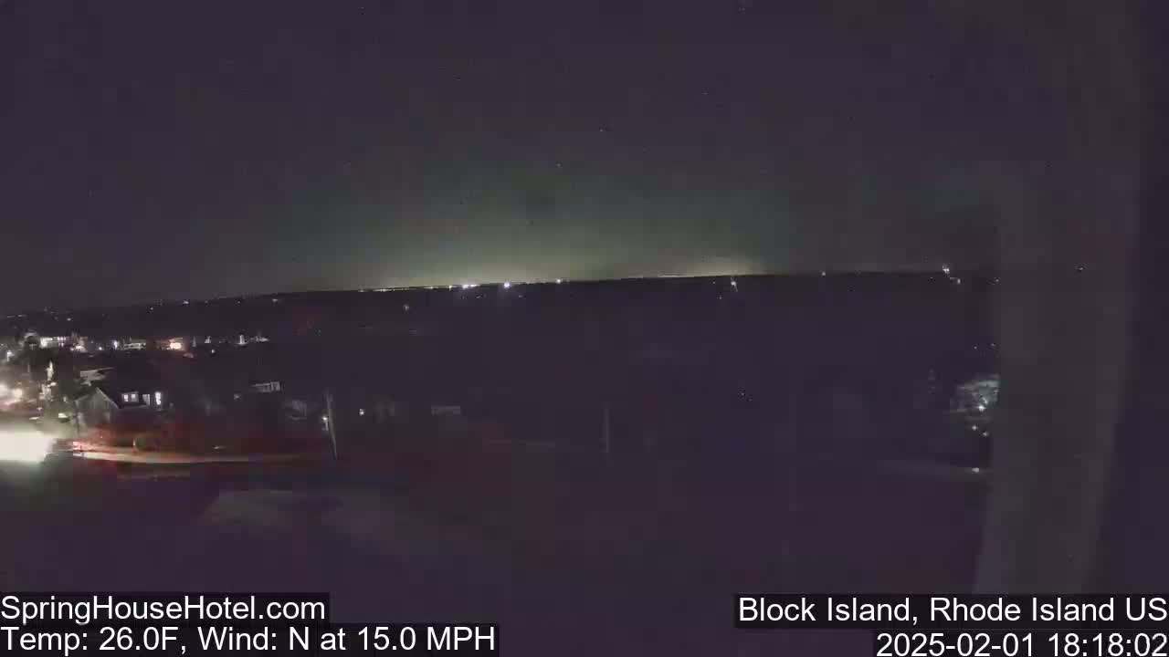 A nighttime view of a town with a dimly lit horizon under a dark sky, with a north wind blowing at 15 mph and a temperature of 26 degrees Fahrenheit.