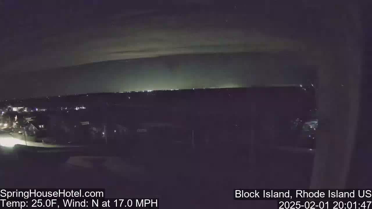 A nighttime view of a town illuminated by lights, under a mostly clear sky with a north wind at 17 mph and a temperature of 25 degrees Fahrenheit.