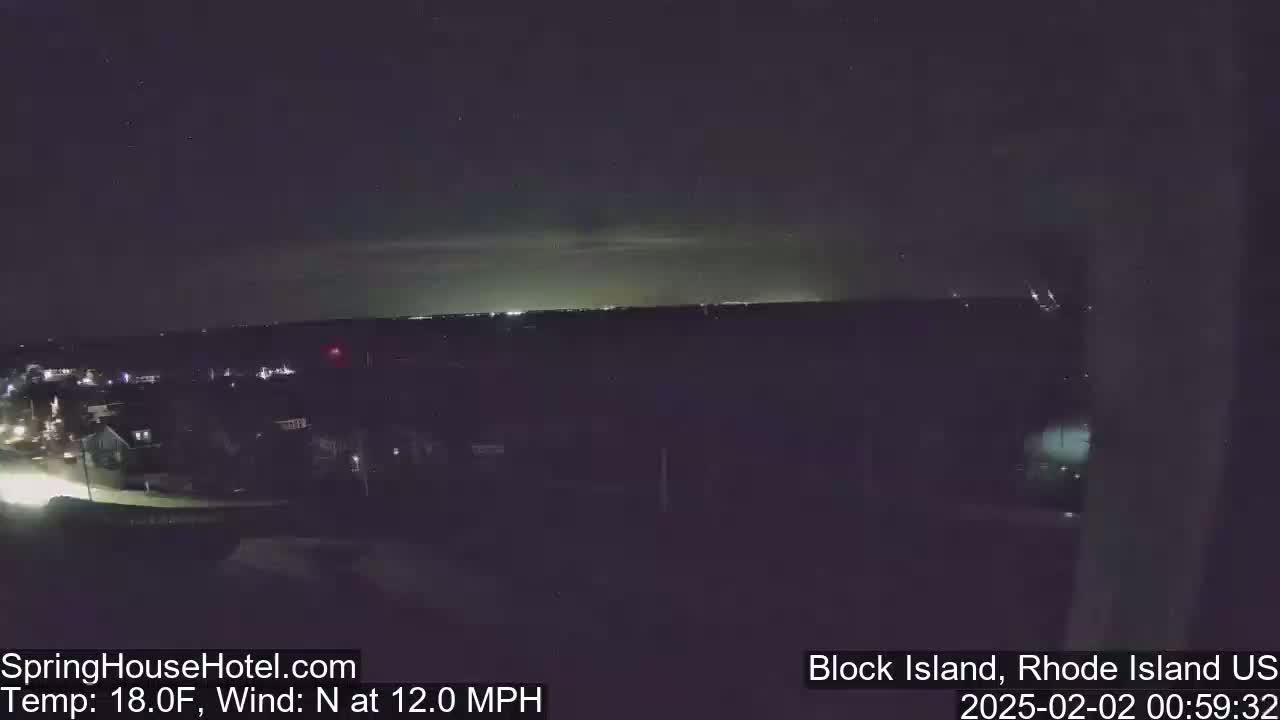 A nighttime view of a town illuminated by streetlights, under a dark sky with a faint glow on the horizon, and a north wind at 12 mph.