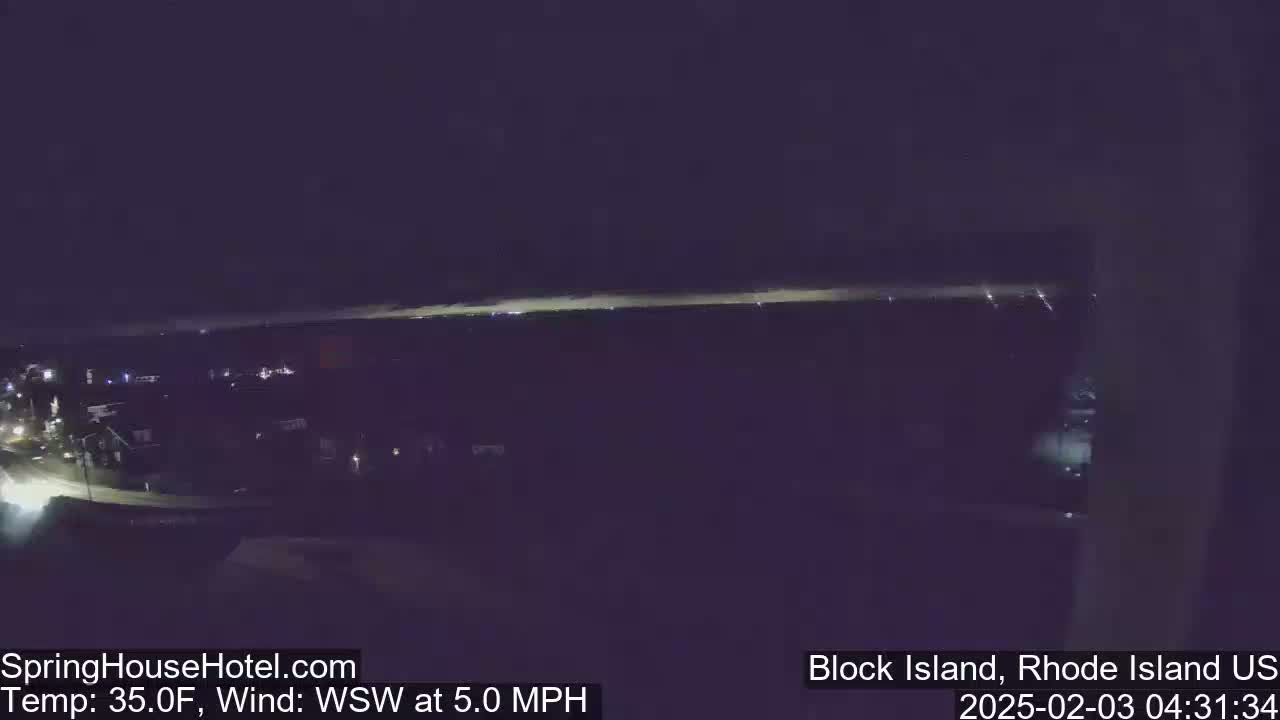 A nighttime, long shot of a dimly lit town next to a dark body of water under a dark sky with a WSW wind at 5.0 mph and a temperature of 35 degrees Fahrenheit.