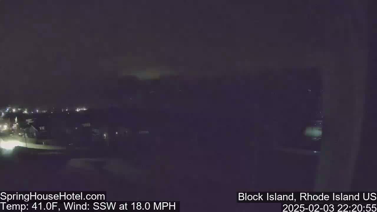A nighttime long shot of a town with dim lights under a dark, cloudy sky, with a south-southwesterly wind blowing at 18 miles per hour.