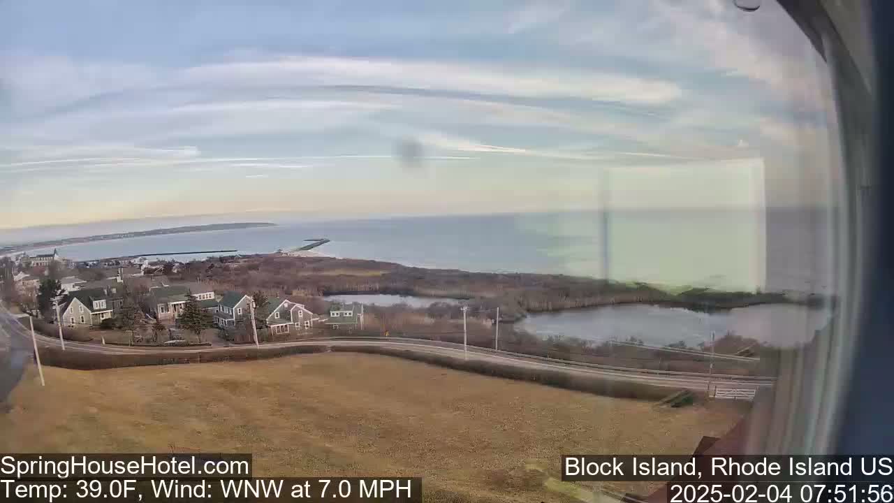 A coastal view shows a calm ocean under a mostly clear sky, with houses and a small pond visible in the foreground.