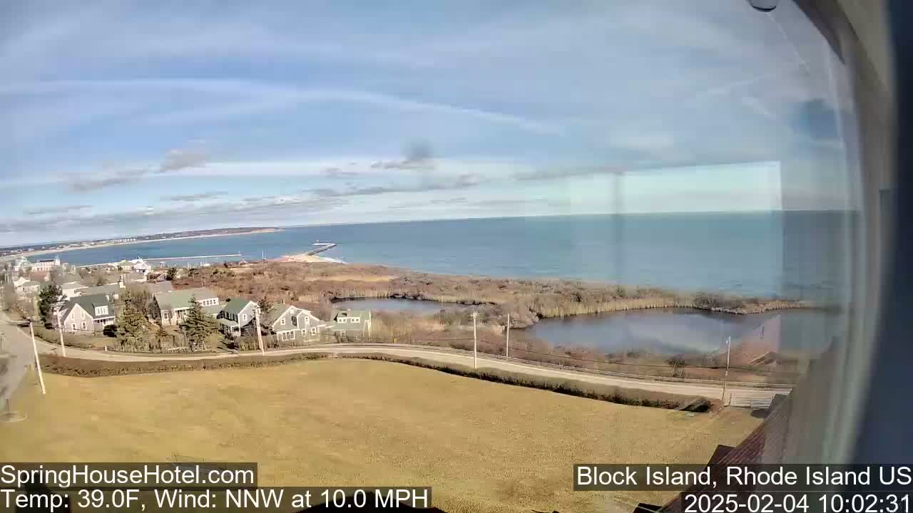 A coastal scene shows a calm ocean under a mostly clear sky, with houses and a pond visible in the foreground.