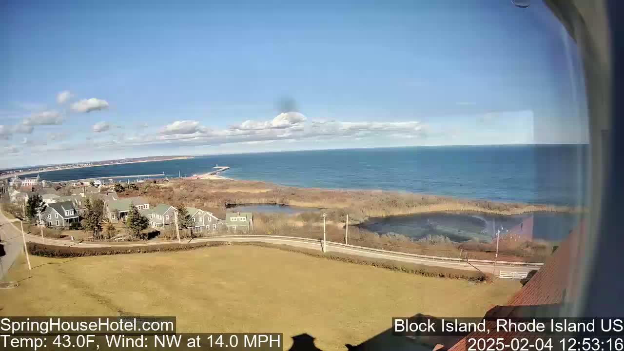 A coastal view on a partly sunny day with a northwest wind of 14 mph shows a residential area overlooking a calm ocean with a breakwater visible in the distance.