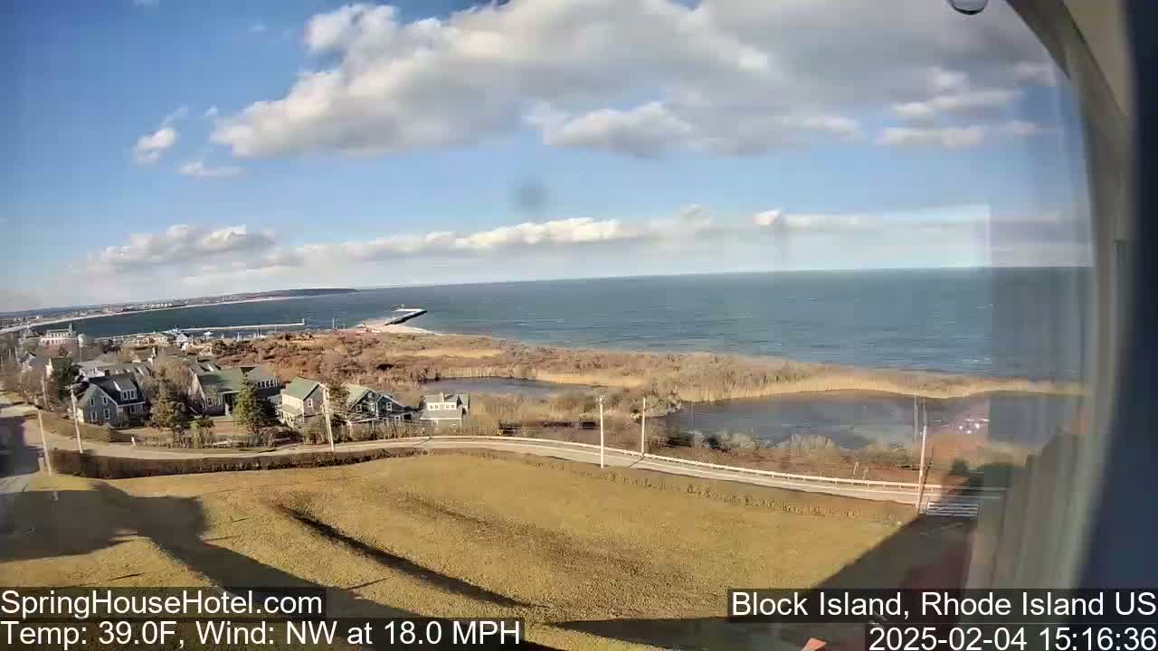 A partly cloudy day with a northwest wind of 18 mph shows a coastal view of houses, marshland, and a calm ocean.