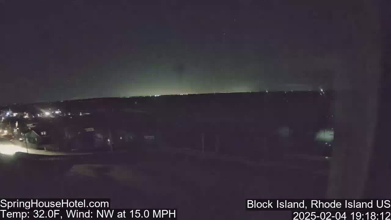 A nighttime view of a town's lights on a horizon under a dark sky, with a northwest wind blowing at 15 mph and a temperature of 32 degrees Fahrenheit.