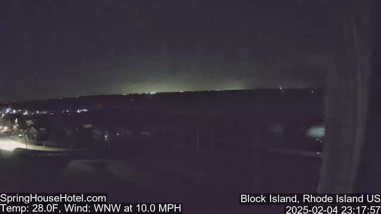 A nighttime, long-range view of a town illuminated by streetlights under a dark sky with a faint light horizon, with a west-northwest wind at 10 mph and a temperature of 28 degrees Fahrenheit.