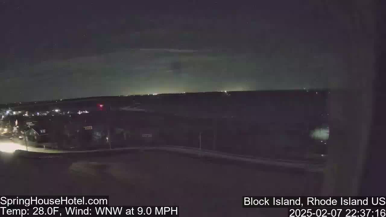 A nighttime long shot of a town with a faint glow on the horizon under a mostly clear sky, with a wind blowing from the west-northwest at 9 miles per hour and a temperature of 28 degrees Fahrenheit.