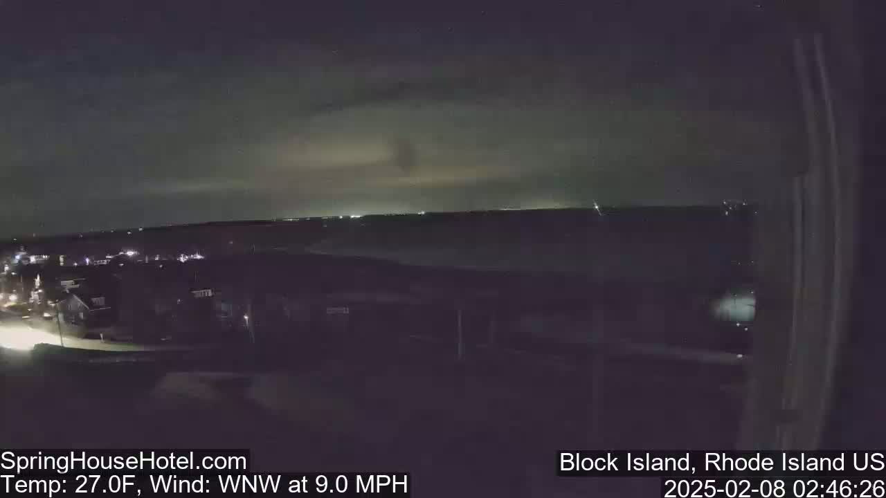 A nighttime, slightly cloudy view of a town with a distant horizon, under a WNW wind blowing at 9.0 mph and a temperature of 27 degrees Fahrenheit.