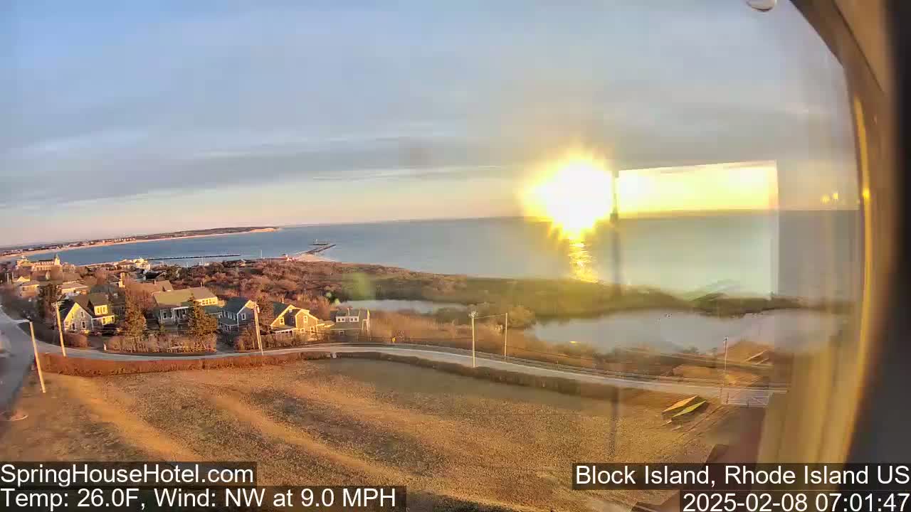 A sunrise over a calm ocean and coastal town with a 26°F temperature and a northwest wind at 9.0 mph.