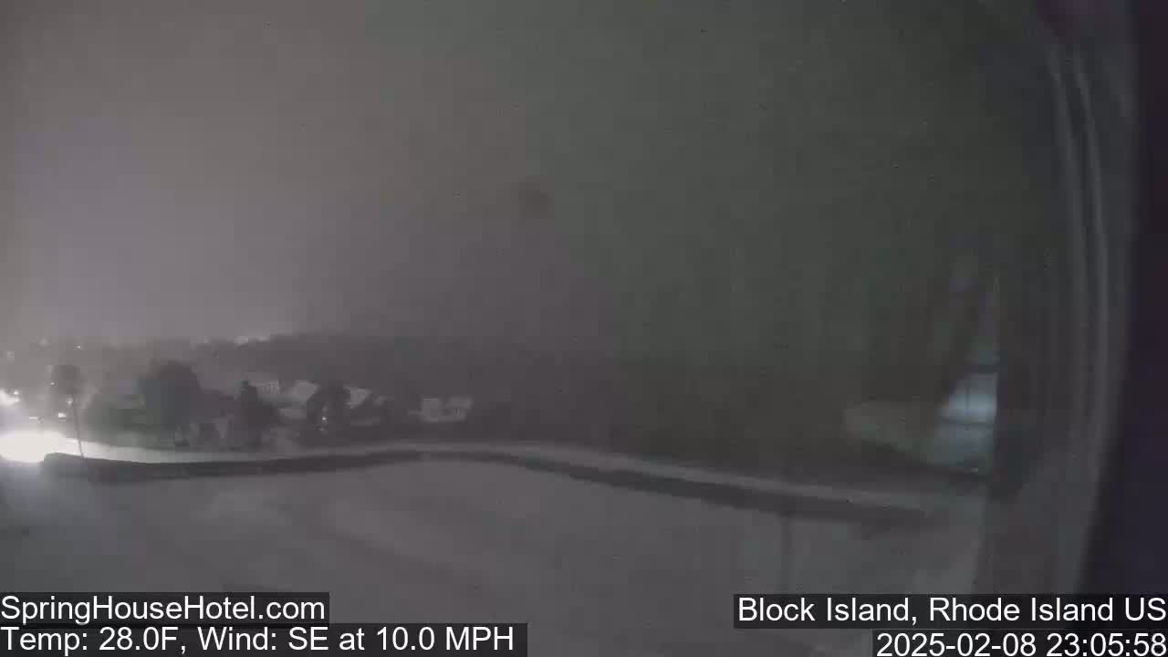 A nighttime, snowy scene shows a road and some buildings barely visible through heavy snowfall with a southeast wind at 10 mph and a temperature of 28 degrees Fahrenheit.