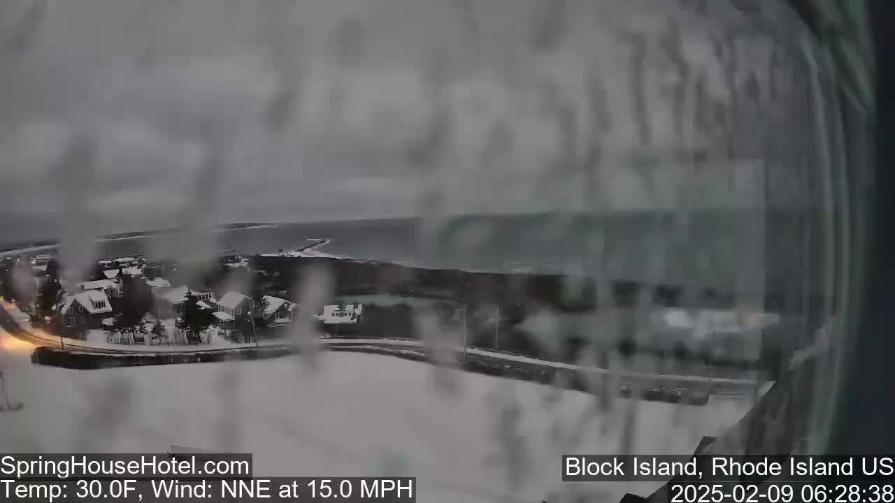 A snow-covered coastal town is viewed from above in overcast conditions, with a 15 mph wind blowing from the north-northeast.