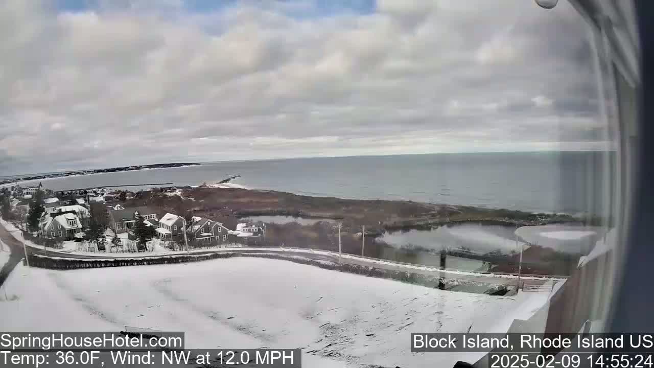 A snow-covered landscape with houses and a calm ocean is visible from a window, under a cloudy sky.