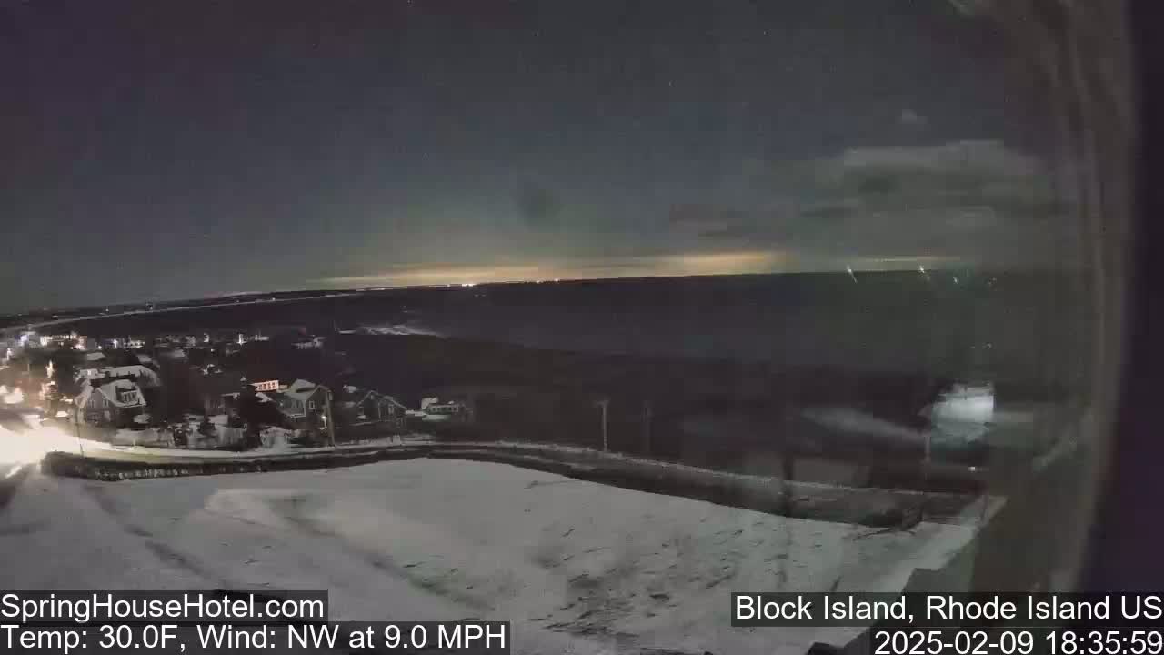 A nighttime view of a snow-covered landscape overlooking a dark ocean under a sky showing a faint aurora.
