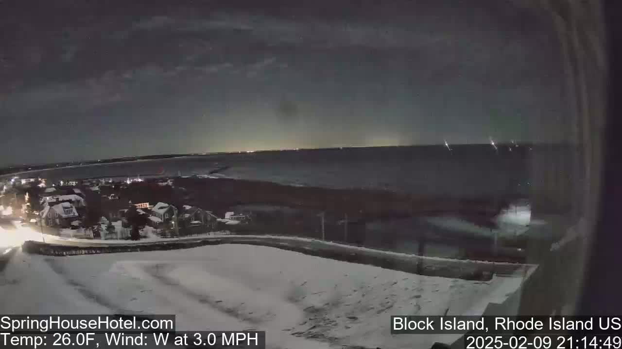 A nighttime, snow-covered landscape overlooks a dark body of water under a partly cloudy sky with a 3.0 mph westerly wind and a temperature of 26°F.