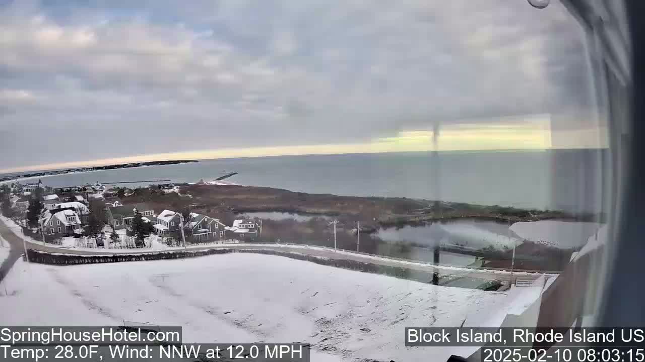 A snow-covered coastal town overlooks a calm ocean under a partly cloudy sky, with a northwest wind blowing at 12 mph.