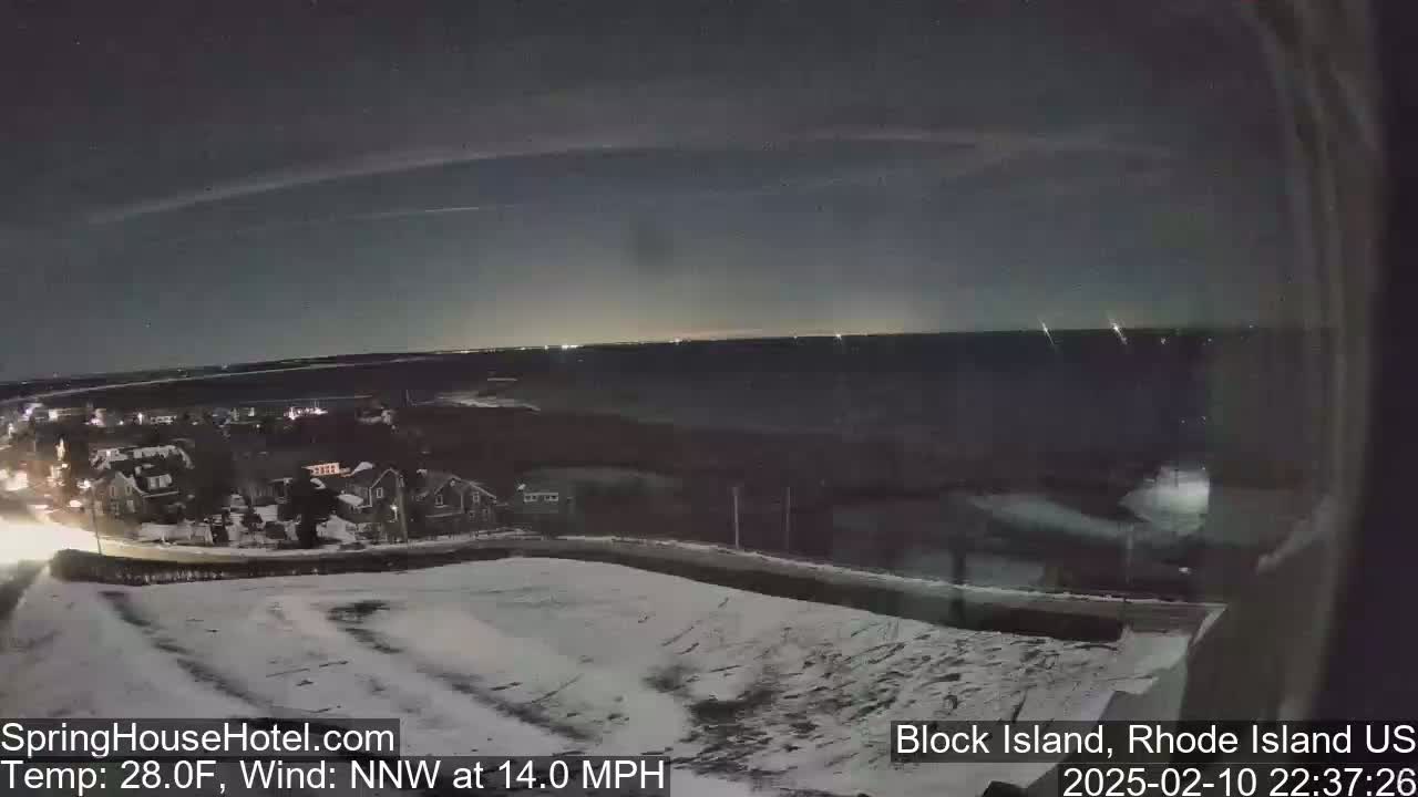 A nighttime view of a snow-covered landscape overlooking a dark body of water under a partly cloudy sky with a northwest wind at 14 miles per hour.